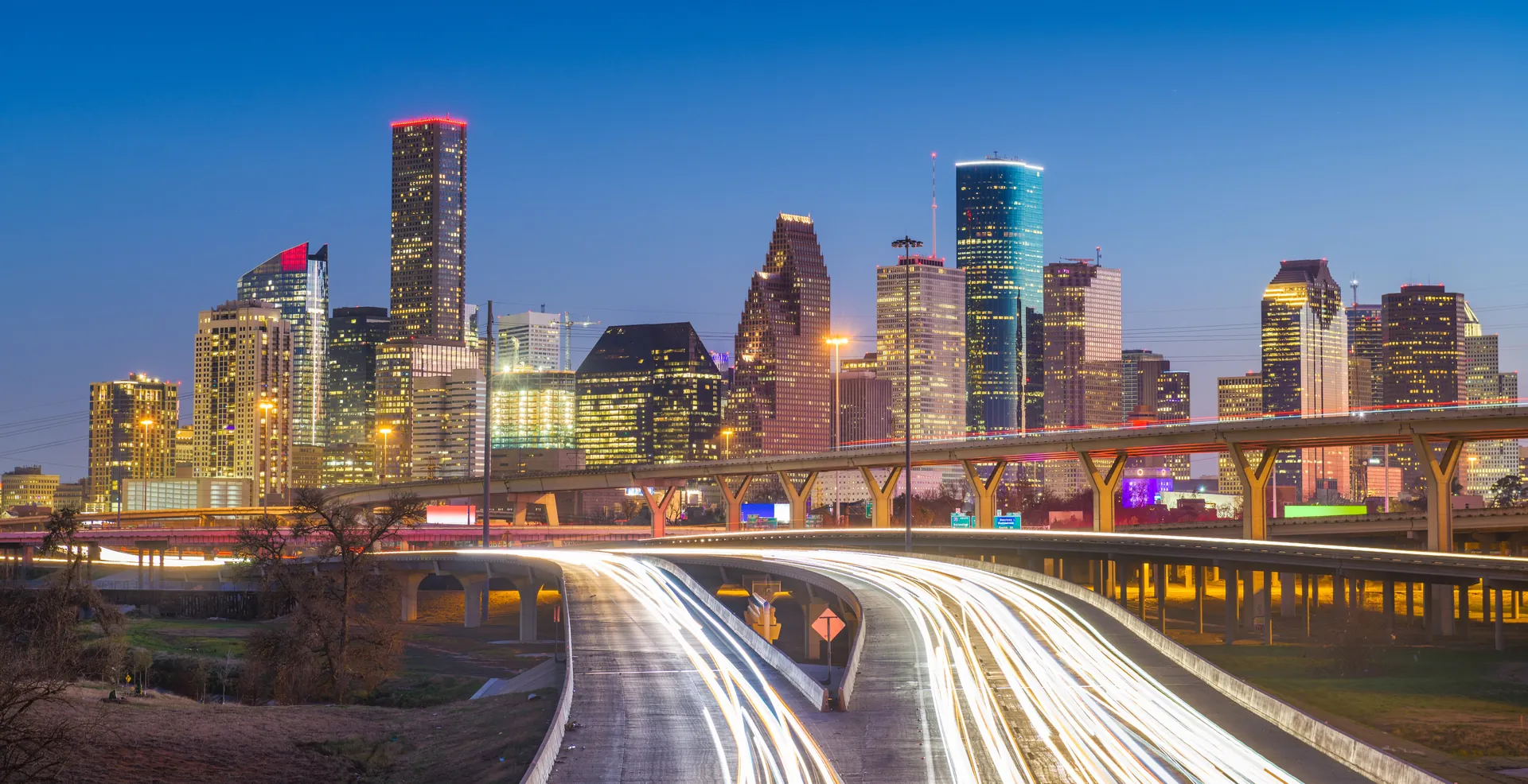 The Houston skyline at dusk, with light trails streaming along the highways below